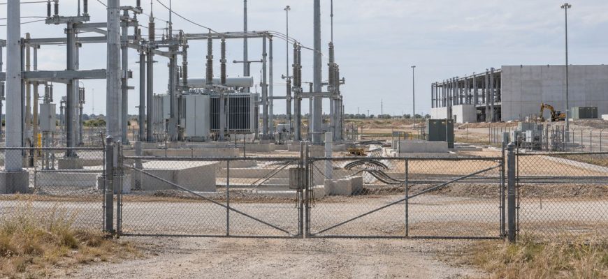 Closed gates at an electrical substation beside a partially built data center site in Texas.