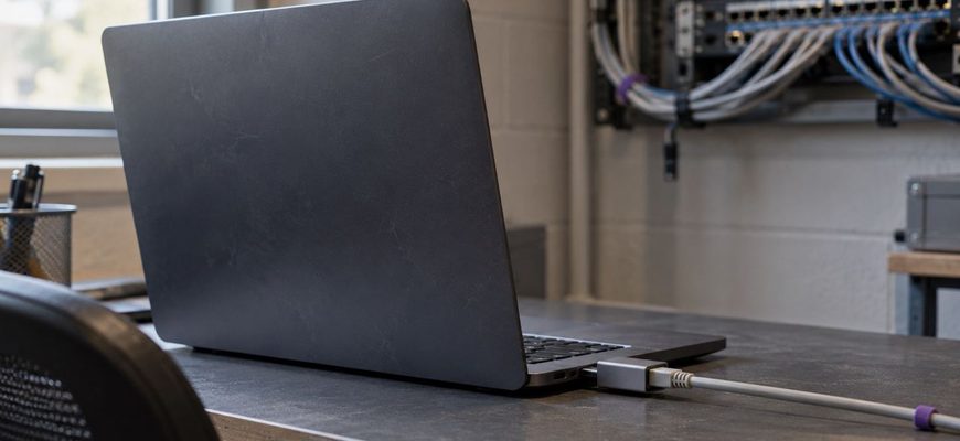 Laptop connected through an Ethernet adapter on a desk, with network equipment in the background.